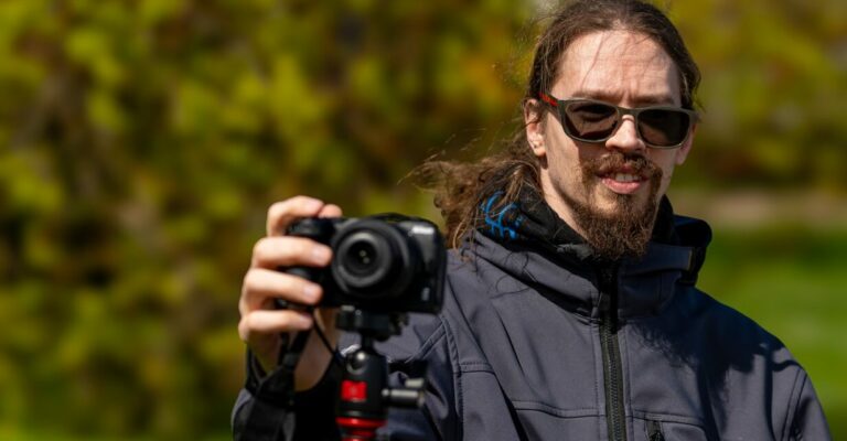 Imelise rohelise looduse taustal seisab päikeseprille kandev meesterahvas. Ta kannab habet ja tal on pikemad juuksed. Tema parem käsi on sirutatud välja Nikon Z30 kaamera päästikule. Ta teeb timelapse. Kaamera on asetatud statiivile.