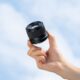 Viltrox AF 56mm F/1.7 Z objektiiv käes taeva taustal, näitab kompaktset suurust